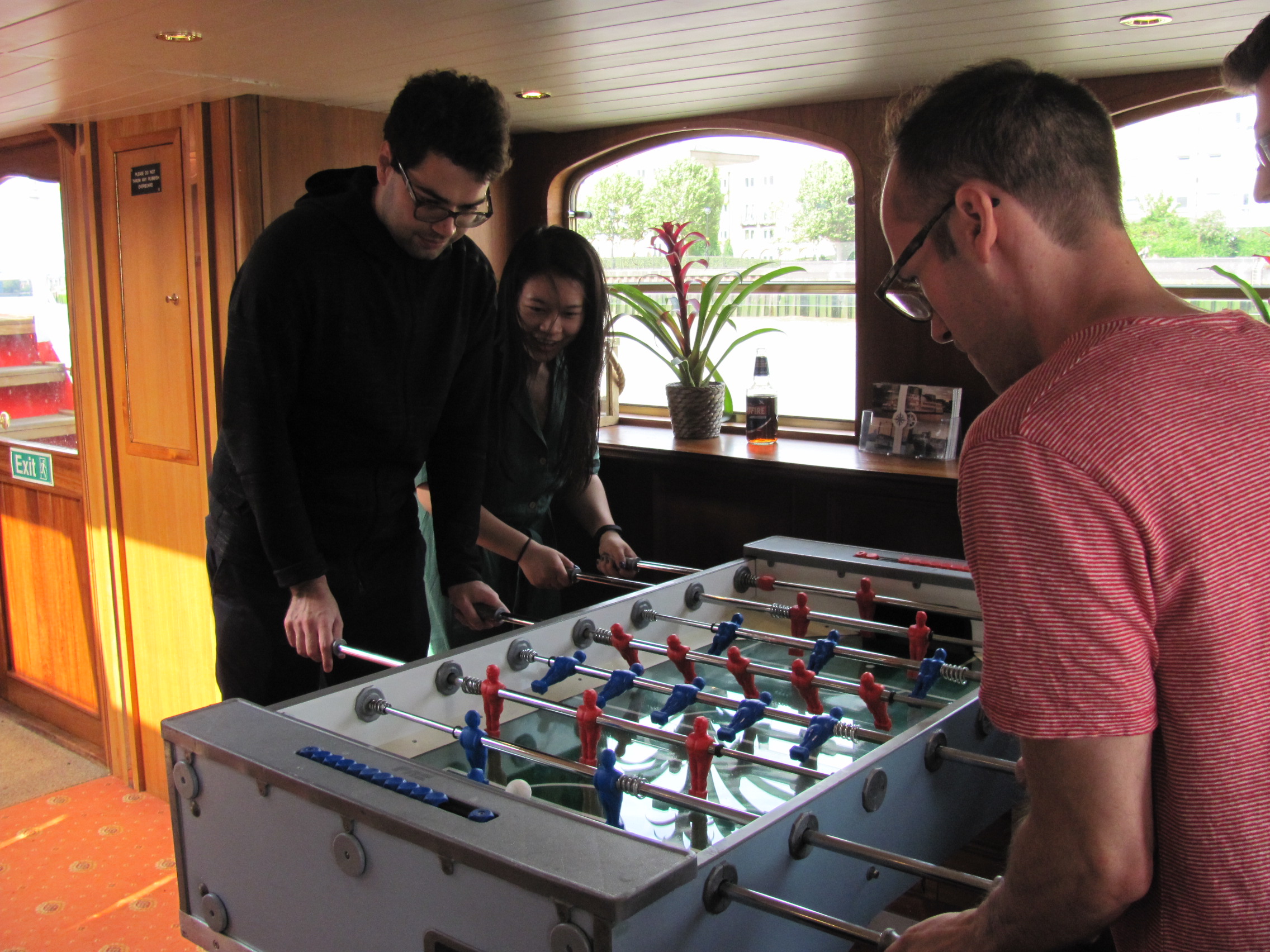 Image 1 shows people playing foosball. Image 2 shows people with rifles on a boat. Image 3 shows people on a boat. Image 4 shows people gathered around dining tables on a boat.