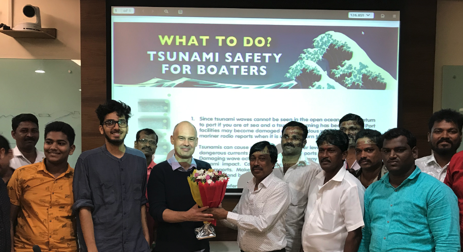 A group of men standing what seems to be an end of a seminar. On the background it reads What to Do? Tsunami Safety for Boaters. There is a man receiving flowers from another in the foreground.