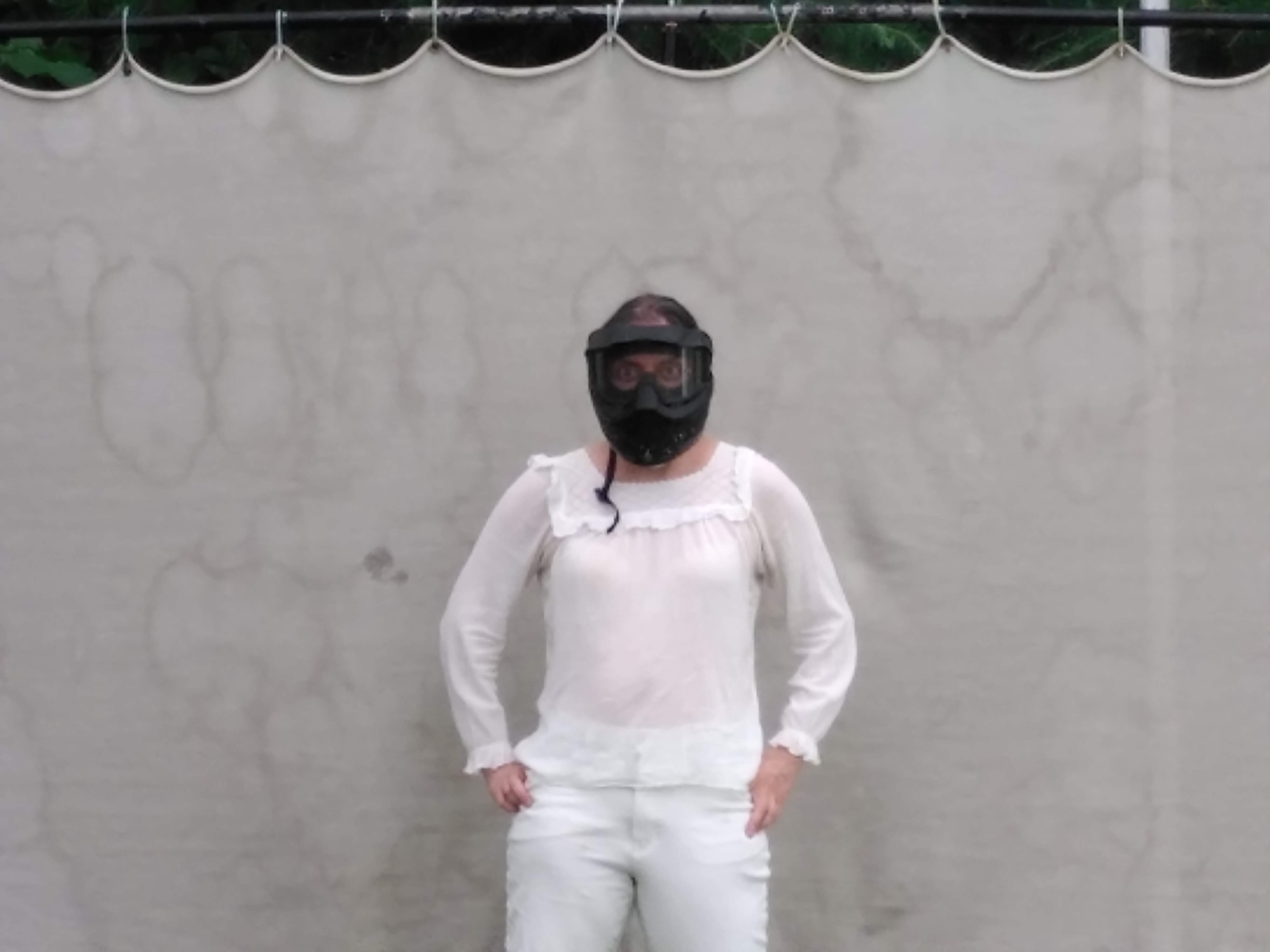 a woman in distance wearing white and in front of a white background. People closer to the screen seem to be aiming at her. In the second image we see a close up of the woman with her face covered with a black helmet.